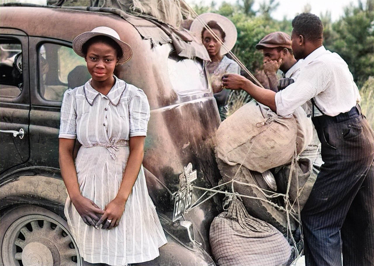 A colourised photograph of travellers beside a loaded car